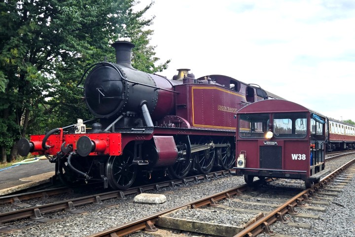 Vintage steam train and small rail car on tracks at a station.