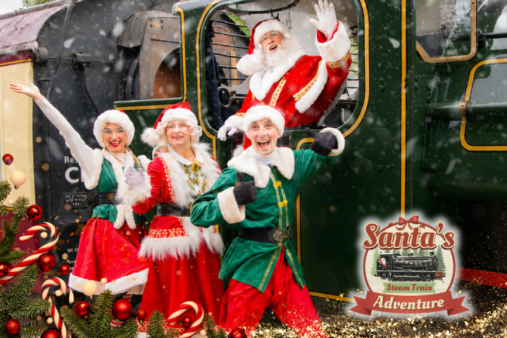 Four people in festive costumes wave from a steam train in snow, with a Santa's Adventure logo.