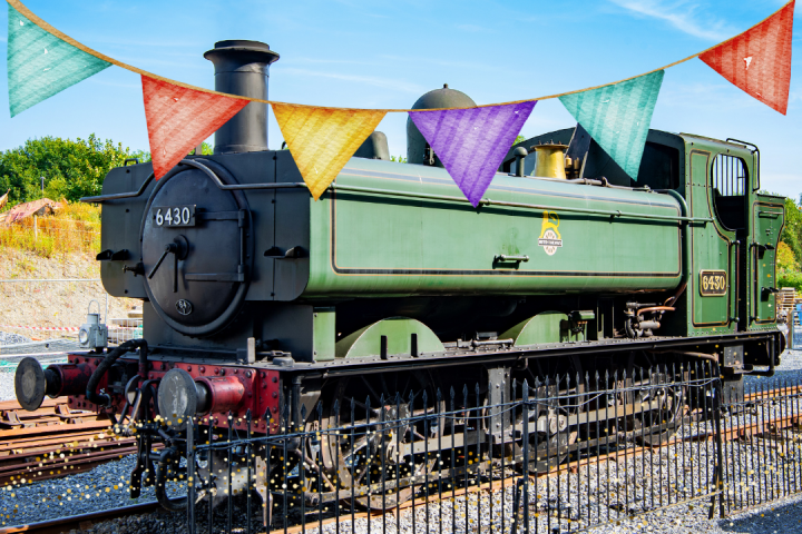 Green steam train number 6430 beside colorful bunting on a sunny day.