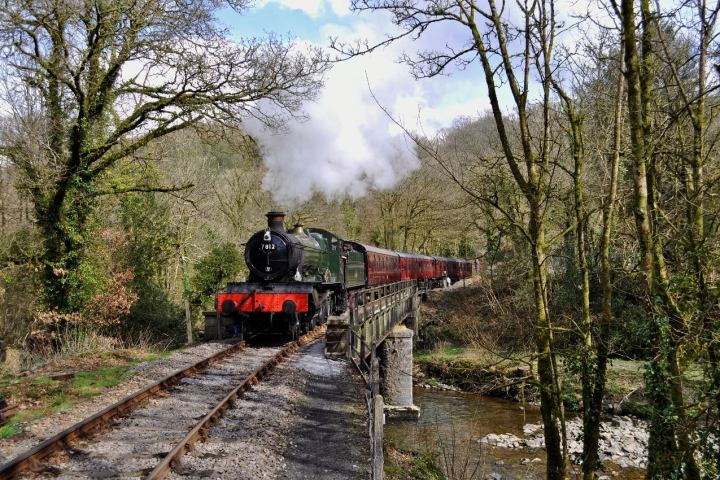 a steam engine train traveling down train tracks near a forest